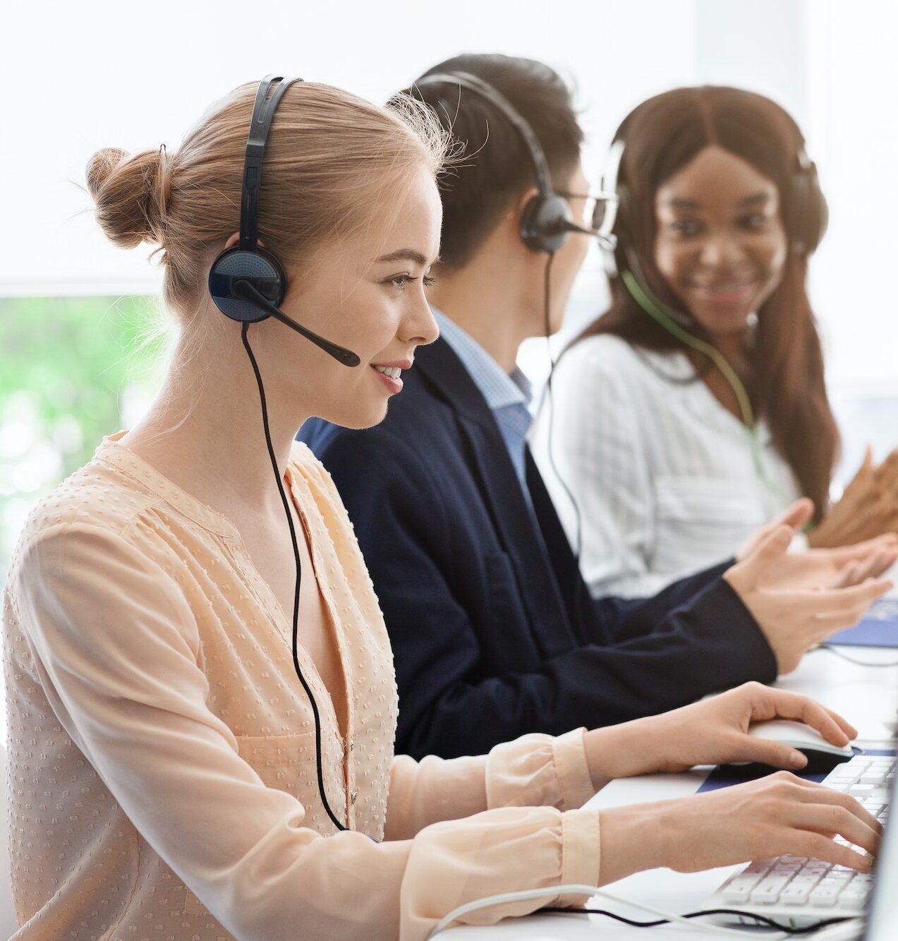 Team of call center operators in headsets speaking with customers at open space office